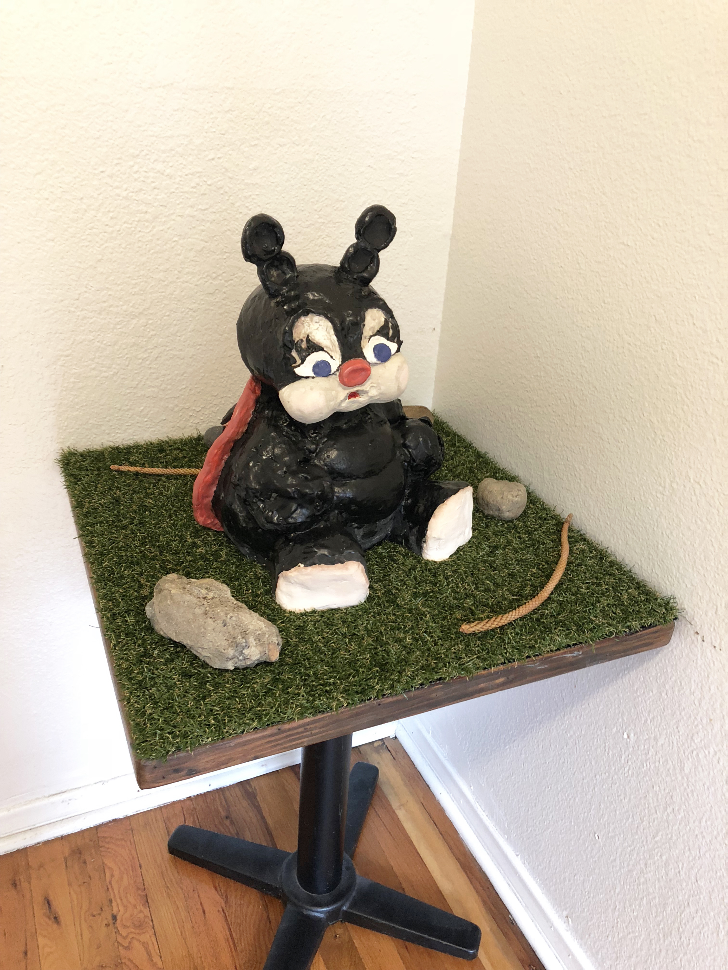 A ceramic sculpture of a black ladybugy on a small table covered in astroturf